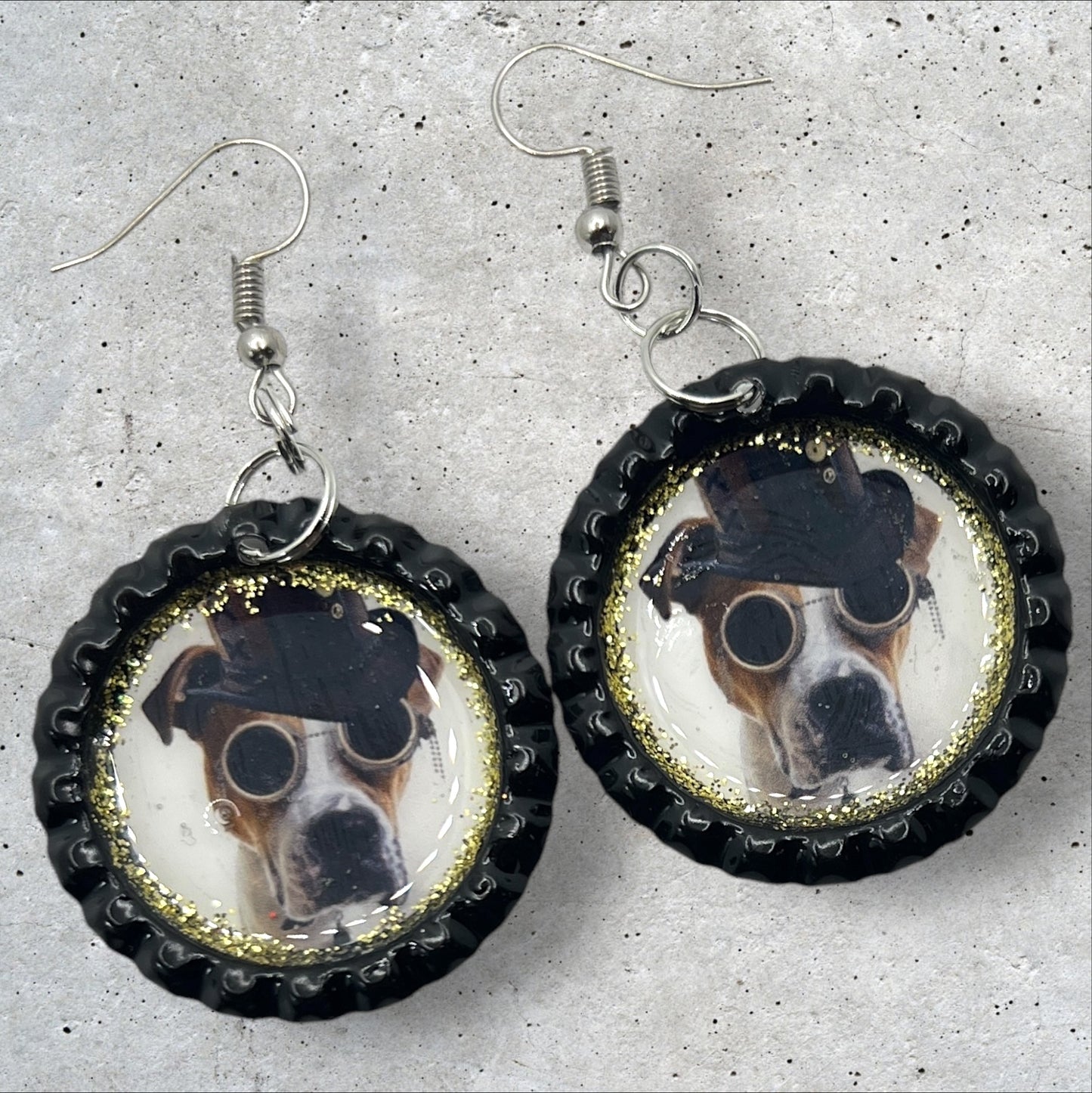 photo of black flattened bottle cap dangle earrings featuring a dog in a black hat and round sunglasses in a steampunk theme surrounded by gold accent glitter