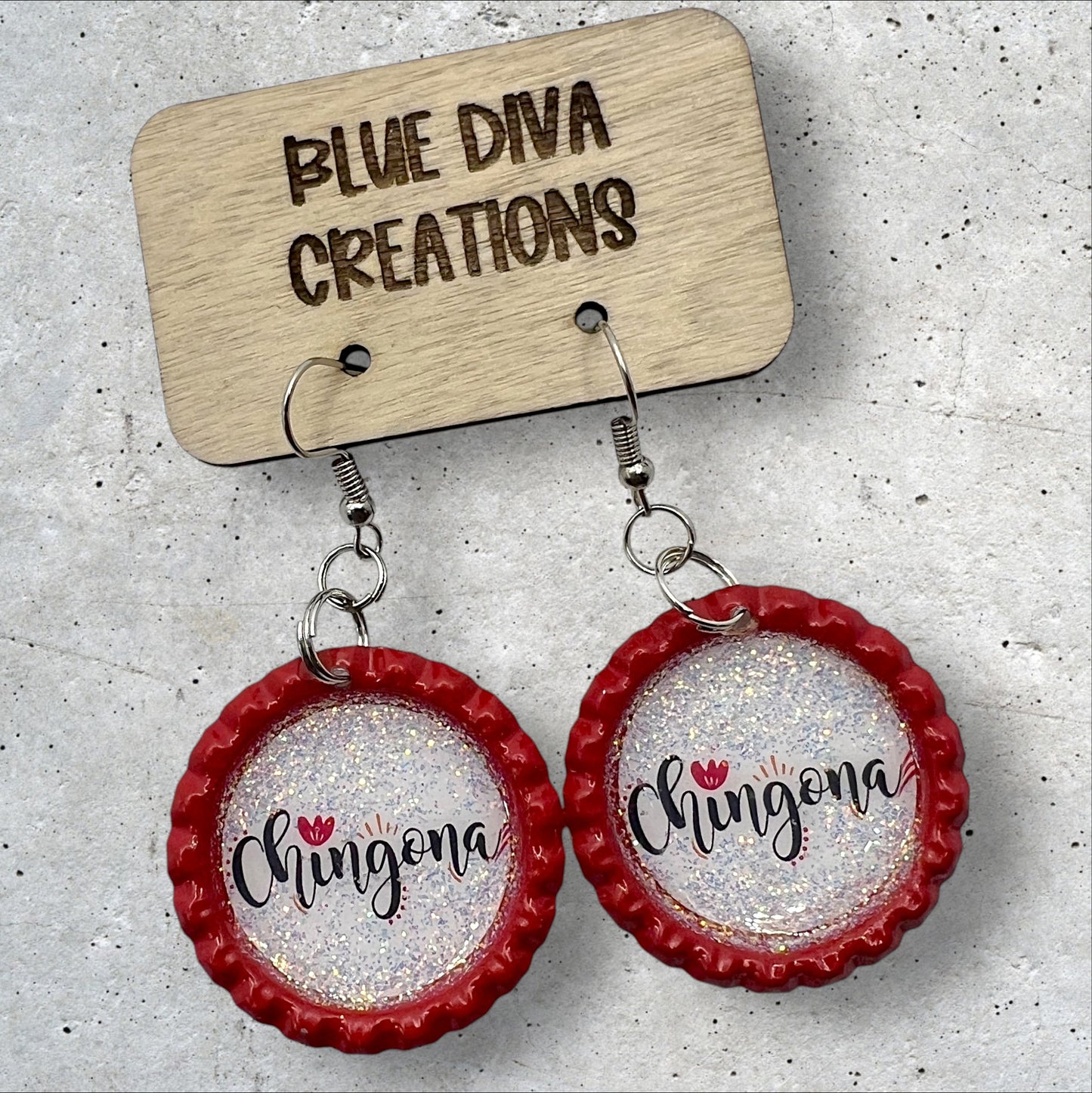 Red flattened bottle cap earrings with script font that says chingona surrounded by iridescent glitter
