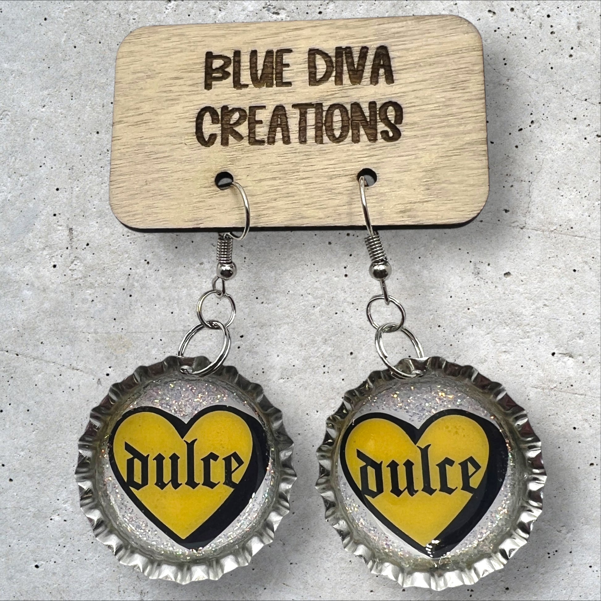 bottle cap earrings with image of a yellow heart with the Spanish words “Dulce” in the middle in gothic font