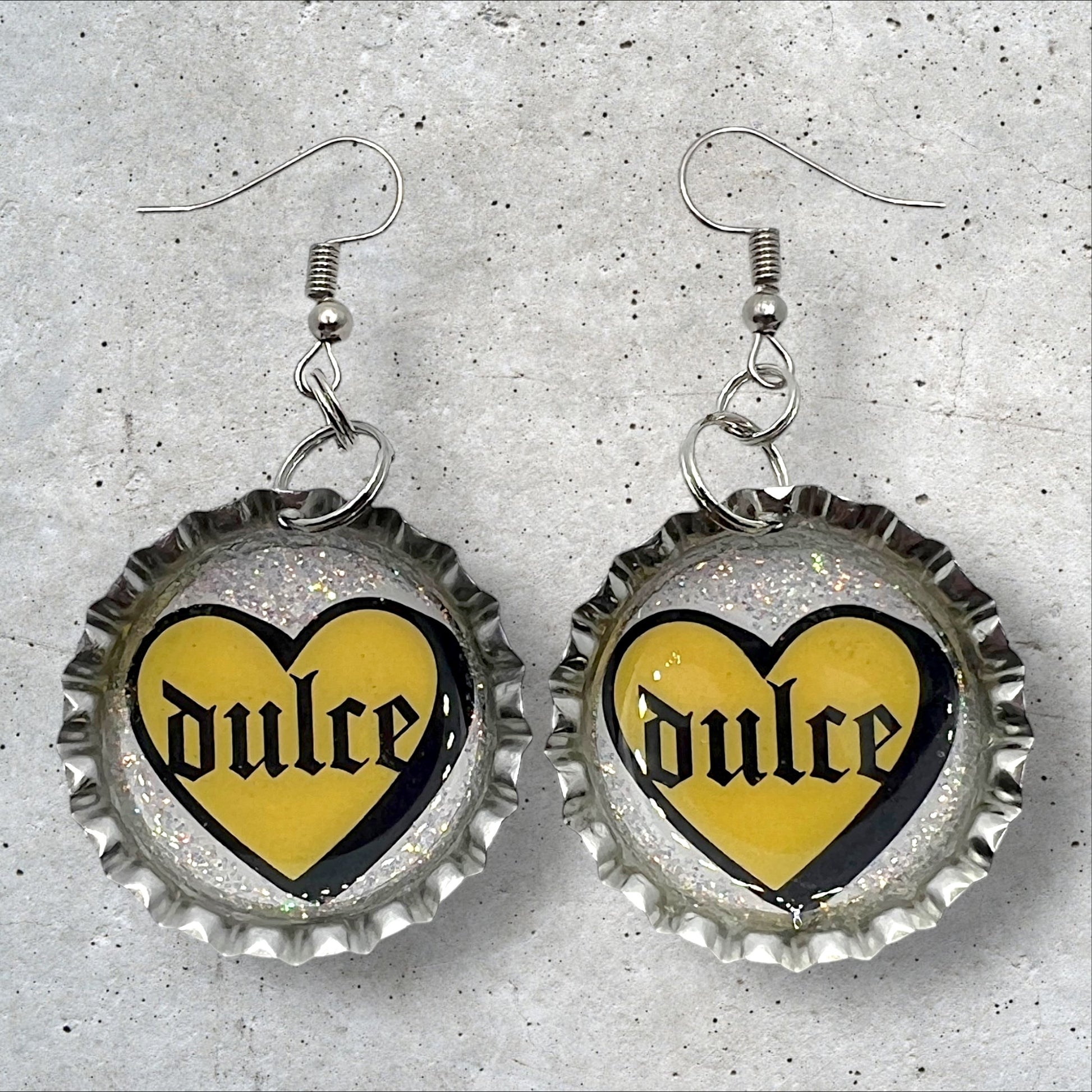 bottle cap earrings with image of a yellow heart with the Spanish words “Dulce” in the middle in gothic font