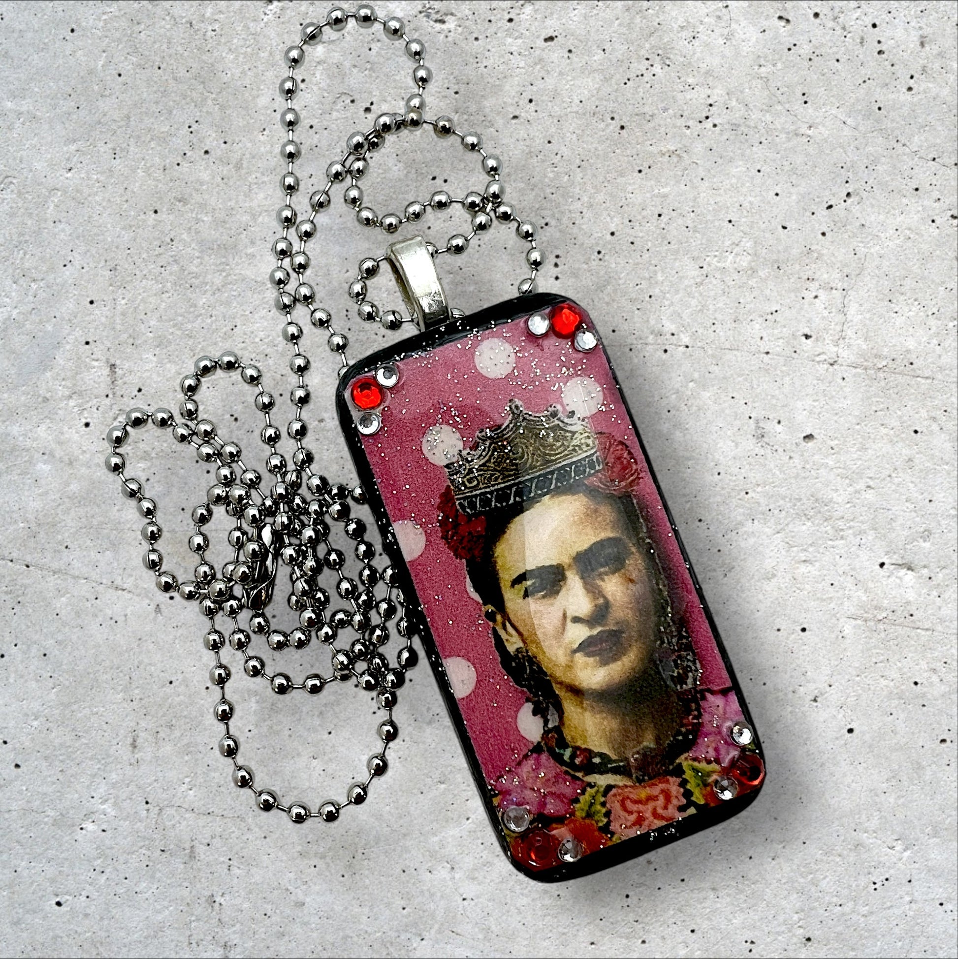 A photo of an upcycled painted domino pendant featuring Frida with a crown on