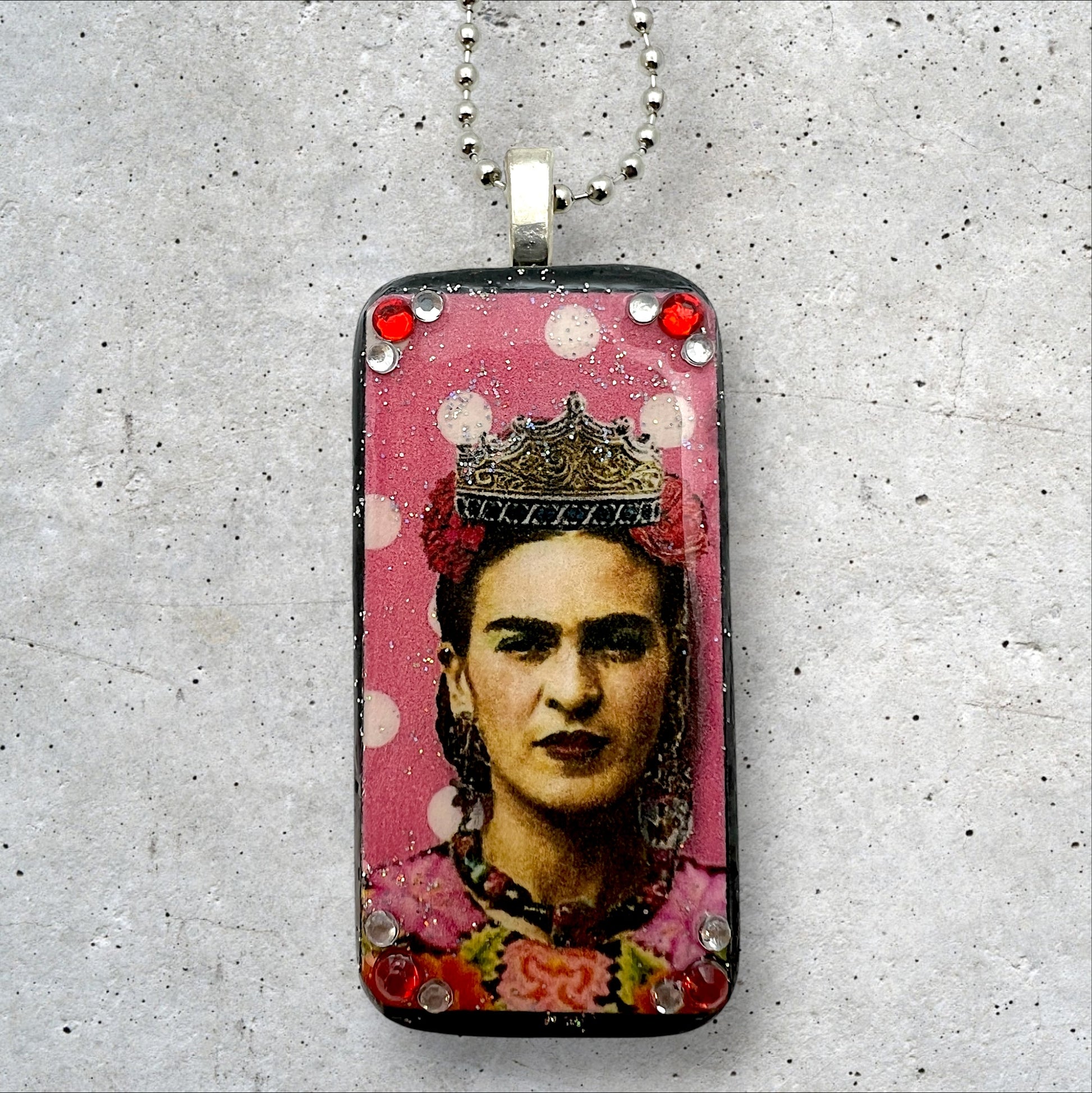 A photo of an upcycled painted domino pendant featuring Frida with a crown on