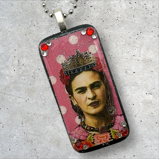 A photo of an upcycled painted domino pendant featuring Frida with a crown on