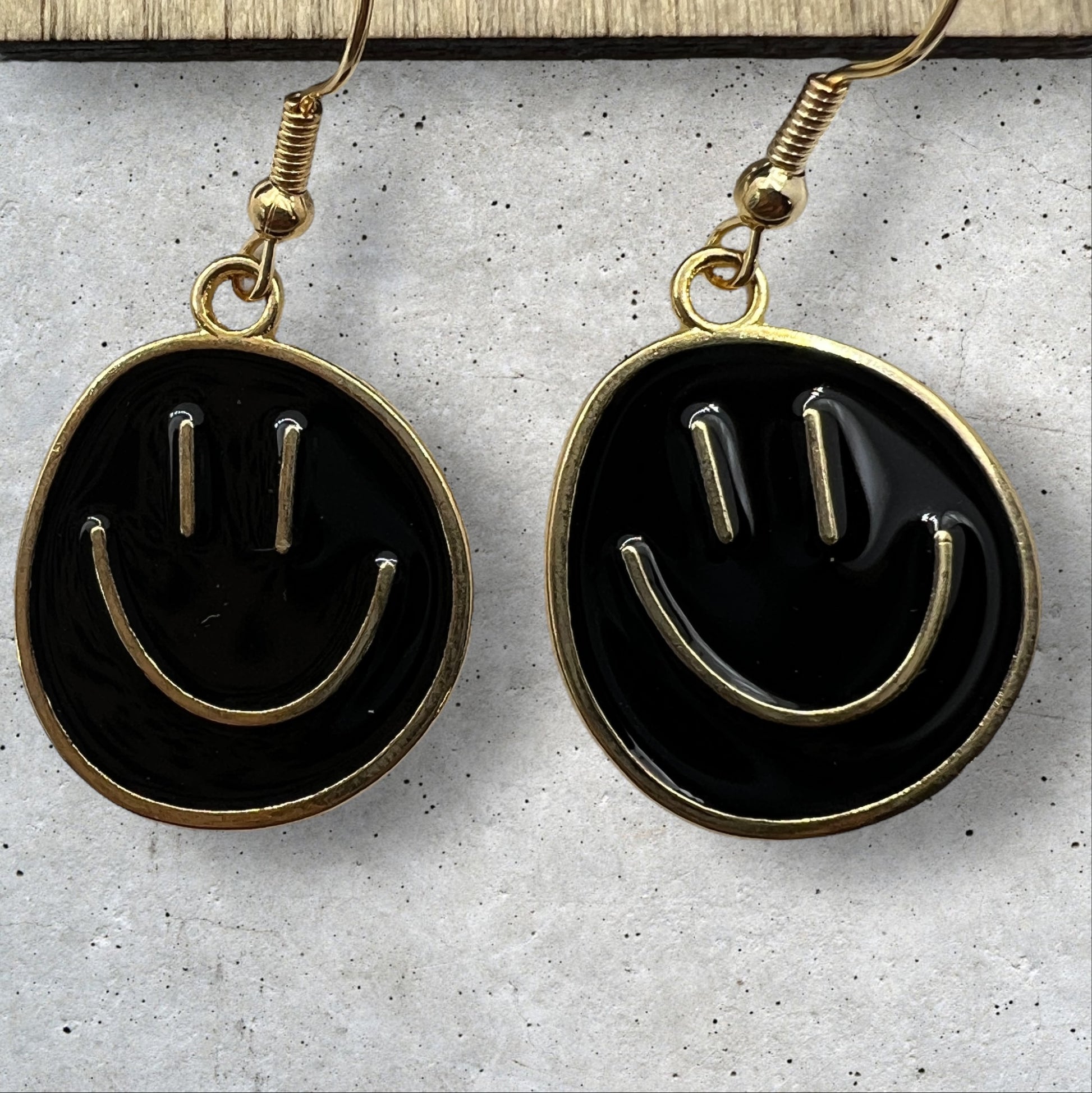 Photo of a pair or round metal black and gold smiley face dangle earrings